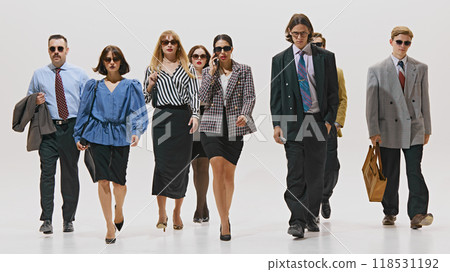 Business professionals, all stylishly dressed in formalwear and sunglasses, walking with purpose against white studio background. 118531192