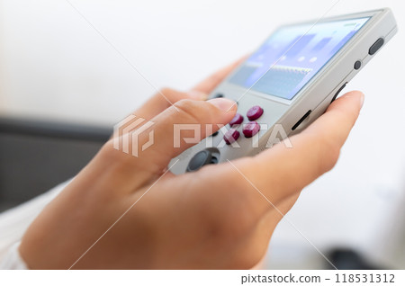 Close-up of female hands of young Caucasian woman holding retro video game console. Girl playing retro games on portable game console. Shallow depth of field. Selective focus Close-up of female hands of young Caucasian woman holding retro video game console. Girl playing retro games on portable game console. Shallow depth of field. Selective focus 118531312
