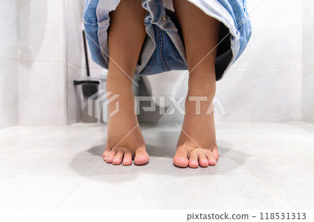 Low angle. A woman sits on the toilet bowl in the bathroom, and she takes off her pants shorts in the bathroom. She had a stomach ache and was dissatisfied with constipation, diarrhea, food poisoning 118531313