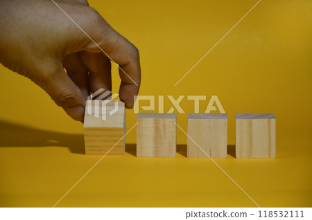 Male hand moving a square wooden block, yellow background. Male hand moving a square wooden block, yellow background. 118532111