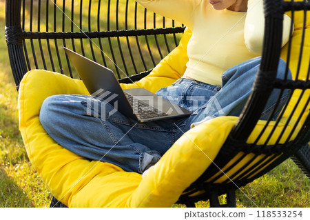 young woman in yellow works at a laptop in a cocoon chair 118533254
