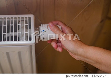 Closeup on woman's hand adjusting thermostat valve in wooden house. High quality photo Closeup on woman's hand adjusting thermostat valve in wooden house. High quality photo 118534250