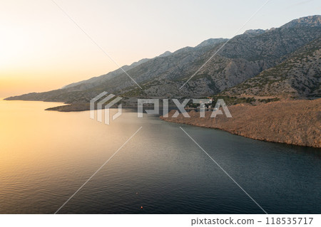 Coastal village among rugged mountains surrounded by sea . Small houses with red-tiled roofs and lush greenery create picturesque scene Coastal village among rugged mountains surrounded by sea . Small houses with red-tiled roofs and lush greenery create picturesque scene 118535717