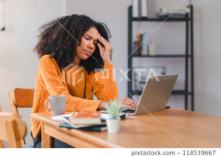 African American woman holding her forehead in frustration while working on a laptop, showcasing stress and exhaustion. African American woman holding her forehead in frustration while working on a laptop, showcasing stress and exhaustion. 118539667