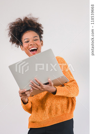 Joyful African American woman celebrating success while looking at laptop, expressing excitement and happiness. Isolated on white background. Joyful African American woman celebrating success while looking at laptop, expressing excitement and happiness. Isolated on white background. 118539668