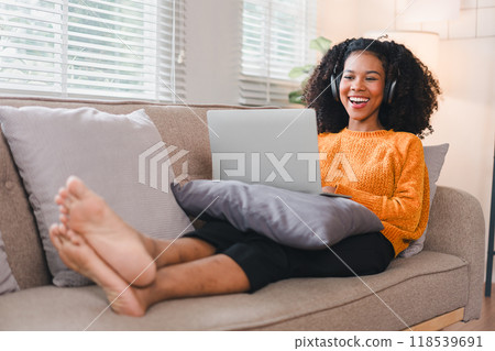 Focused African American woman using laptop while sitting comfortably on a couch. 118539691