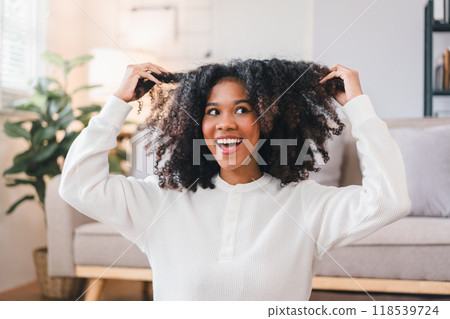 Smiling African American Woman Fluffing Her Curly Hair Indoors. 118539724