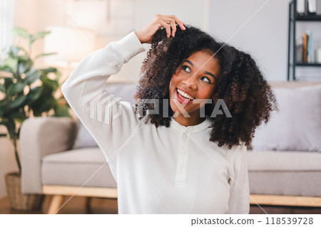 Excited African American Woman Playing with Curly Hair at Home. 118539728