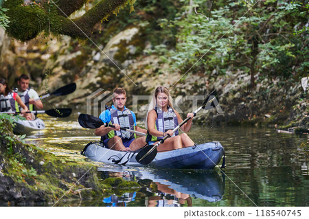 A young couple enjoying an idyllic kayak ride in the middle of a beautiful river surrounded by forest greenery A young couple enjoying an idyllic kayak ride in the middle of a beautiful river surrounded by forest greenery 118540745