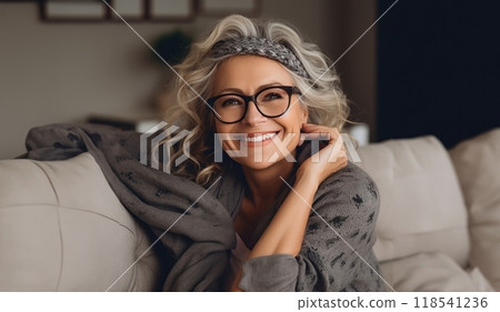 In her sunlit living room, the modern elderly woman exudes sophistication, wearing glasses, creating a chic and cozy atmosphere. 118541236