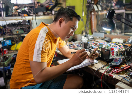 Repair man looks at the circuit and takes notes on the workbench Repair man looks at the circuit and takes notes on the workbench 118544574