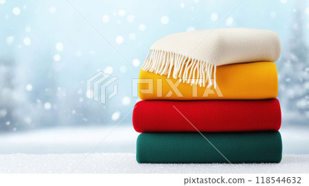 Cozy stack of colorful blankets in winter setting, perfect for warmth and comfort during cold days. vibrant colors add cheerful touch to snowy backdrop 118544632