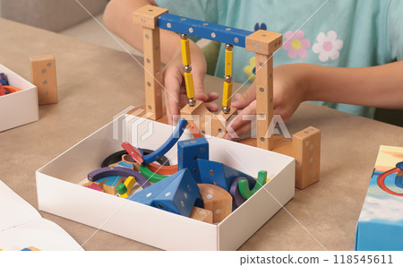Girl assembles swing from magnetic wooden construction set. Toys and activiti children. Developmental activities at home.  118545611
