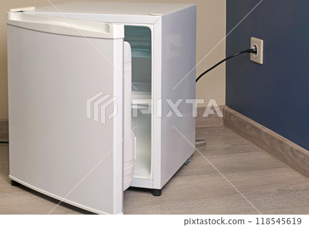 Single chamber empty white open mini fridge with freezer above on floor. Home appliances. Food and food storage at home.  118545619