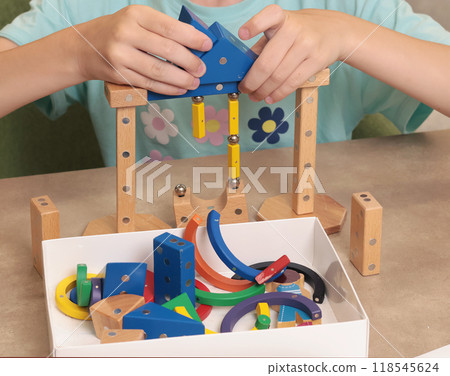 Girl assembles swing from magnetic wooden construction set. Toys and activiti children. Developmental activities at home.  118545624