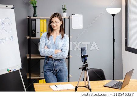 Young woman mentor recording presentation, webinar on smartphone standing on tripod, teacher coach explaining, holding online lesson, using phone webcam. 118546327