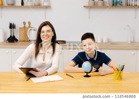 A young woman helps a boy with his lessons using a tablet and a globe. A homeschooling student does his homework with the help of a tutor 118546908
