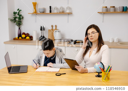 A young woman helps a boy with his lessons using a tablet and a globe. A homeschooling student does his homework with the help of a tutor A young woman helps a boy with his lessons using a tablet and a globe. A homeschooling student does his homework with the help of a tutor 118546910