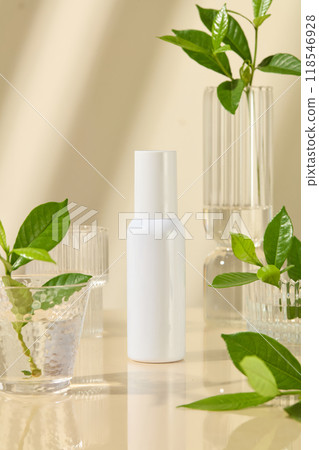 Cosmetic mockup for promotional, a blank label white cosmetic bottle placed in center, surrounded by different types of glass jar with water and green plants in. Beige background 118546928