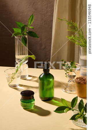 Advertising mockup of organic skincare product with an unlabeled shampoo bottle and a green moisturizer pot placed side by side on light yellow table, spa theme items decorative 118546948