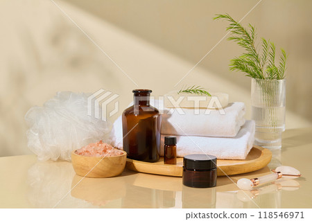 Photo of spa concept was taken from front view, some unbranded cosmetic containers placed on wooden tray with white bath towels and soap, glass jar with green plant decorated in back 118546971