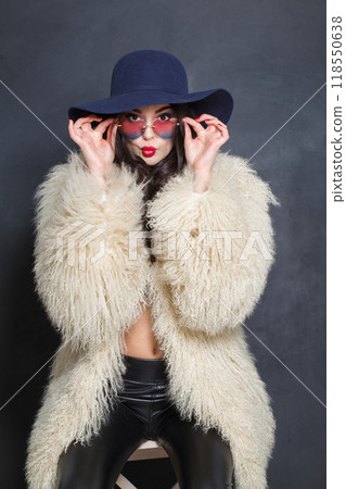 Funny fashion model woman in blue classic hat and white fur coat posing indoor Funny fashion model woman in blue classic hat and white fur coat posing indoor 118550638