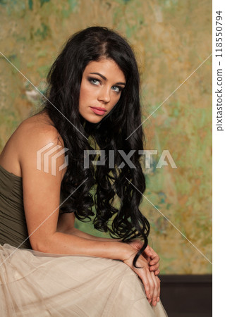 Young brunette woman posing in art studio. Young lady with long curly hair and make-up Young brunette woman posing in art studio. Young lady with long curly hair and make-up 118550794