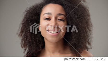Beauty and healthcare concept - beautiful African American woman with curly afro hairstyle and clear, healthy skin looks at the camera with a calm gaze and smiles a bright toothy smile Beauty and healthcare concept - beautiful African American woman with curly afro hairstyle and clear, healthy skin looks at the camera with a calm gaze and smiles a bright toothy smile 118551342