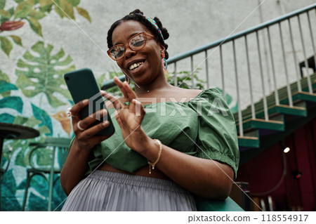 Low angle shot of smiling African American woman chatting on social network with friend Low angle shot of smiling African American woman chatting on social network with friend 118554917