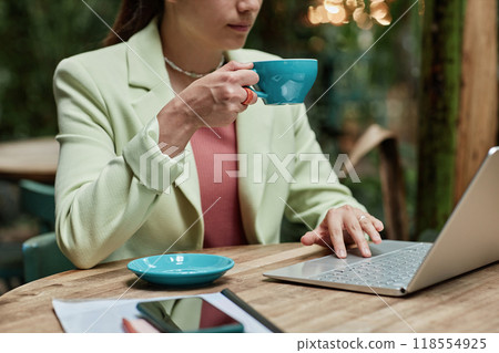 Unrecognizable woman holding turquoise coffee mug and working via laptop in cafe 118554925