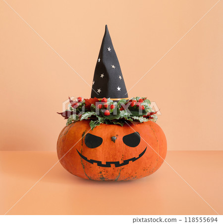 Jack o lantern pumpkin head with flowers in black witch hat on beige background. Halloween funny pumpkin. 118555694