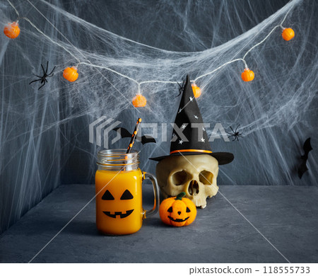 Halloween party decorations. Pumpkin juice with scary face, cobwebs and skull on blue background. Halloween drink. Halloween party decorations. Pumpkin juice with scary face, cobwebs and skull on blue background. Halloween drink. 118555733