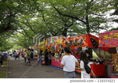 At the festival stalls, people enjoy eating as they please, walking around in the sunlight filtering through the cherry blossom trees. 118555821