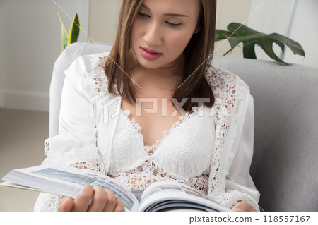 A woman in a silk nightgown reads a magazine leisurely. 118557167