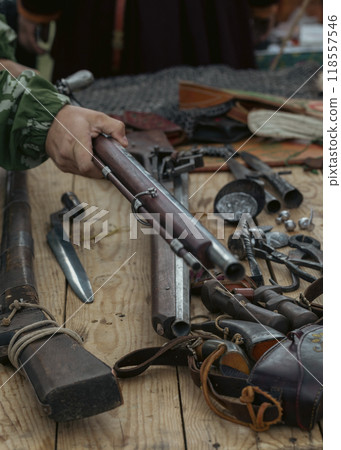 Set of antique firearms, bayonets, saber and peak tips on wooden table. Human hand holds a rifle, selective focus. 118557546