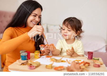 smiling little girl and mother spending good time painting hands and autumn yellow leaves together 118558291