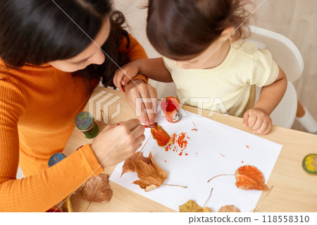 happy little child girl and her mother drawing for the autumn holiday. happy family painting autumn leaves happy little child girl and her mother drawing for the autumn holiday. happy family painting autumn leaves 118558310