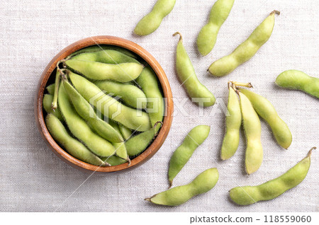 Fresh edamame, green soybeans in the pod, in a wooden bowl, on linen. Raw immature soybeans, Glycine max, used boiled or steamed and salted, as a common side dish and appetizer in Japanese cuisine. 118559060