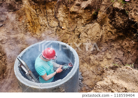 Worker makes hole for an inlet pipe in concrete septic tank ring using an abrasive wheel and an angle grinder. 118559404