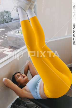 Woman wears yellow blue fitness outfits do Lying Bench Leg Raise in he gym. Woman wears yellow blue fitness outfits do Lying Bench Leg Raise in he gym. 118561469