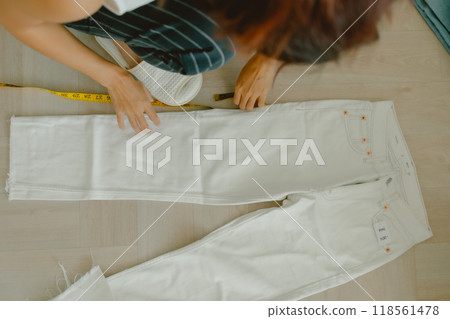 Woman is measuring her white jean on the floor of the room. Woman is measuring her white jean on the floor of the room. 118561478