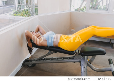 Woman wears yellow blue fitness outfits do Lying Bench Leg Raise in he gym. Woman wears yellow blue fitness outfits do Lying Bench Leg Raise in he gym. 118561479
