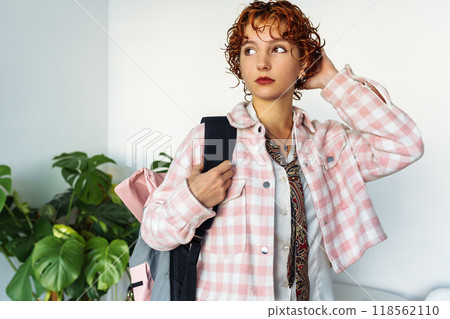 attractive extravagantly dressed young woman, student, schoolgirl with red curly hair with backpack in home interior attractive extravagantly dressed young woman, student, schoolgirl with red curly hair with backpack in home interior 118562110