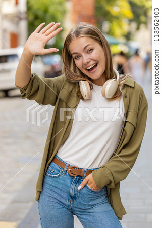 Caucasian woman smiling friendly at camera, hello waving hands gesturing hi, greeting on city street Caucasian woman smiling friendly at camera, hello waving hands gesturing hi, greeting on city street 118562403