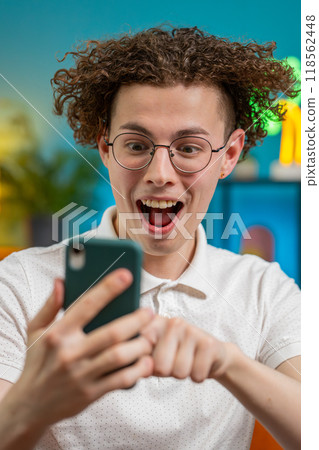 Surprised excited man holding smartphone reading good news amazed by online game casino lottery win 118562448