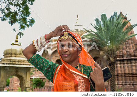 Indian Woman with beautiful face and orange sari posing with ruins in background Indian Woman with beautiful face and orange sari posing with ruins in background 118563010