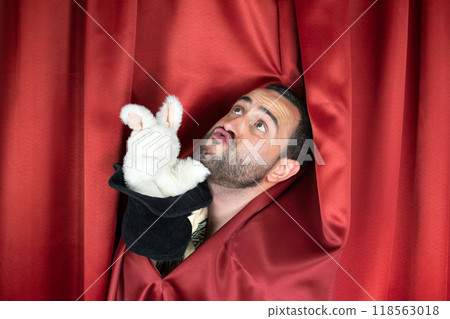 Funny young adult man magician with Punch face playing with evil rabbit out hat 118563018