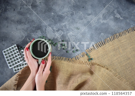 A cup of green seaweed powder in the hands of a young girl 118564357