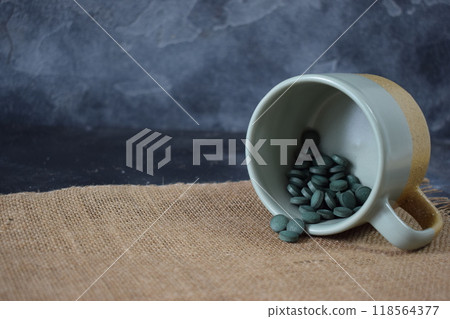 Green seaweed powder, pills and capsules in a cup on a black background Green seaweed powder, pills and capsules in a cup on a black background 118564377