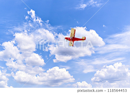 Red single-engine ultralight airplane flying in the blue sky with white clouds	 118564453